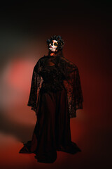 Woman in black costume and cartina makeup standing with closed eyes on burgundy background.