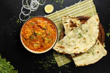 Paneer Butter Masala served with naan bread,onion rings and lemon, on a black background with space...