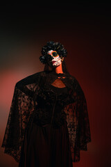 Fototapeta na wymiar Woman in santa muerte halloween costume standing on burgundy background.