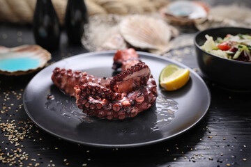 Grilled octopus tentacles on a black plate, on a wooden table. Mediterranean, fish restaurant delicacy.