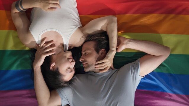 Top view of diverse young men lying on rainbow flag and cuddling