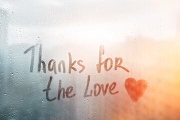Handwritten text Thanks for love written finger with heart shape on orange sunset wet window