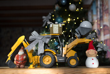 concept of christmas business greetings, new year winter holidays in construction company. toy bulldozer - excavator, gift box, figurine of Santa Claus, snowman against of a decorated Christmas tree © Anna
