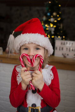 cute child in red santa hat, holding heart-shaped lollipops in front of his face. kid is waiting for a miracle on Christmas Eve. New Year, merry winter holidays. Festive mood. Santa's little helper