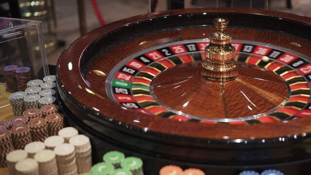 Spinning roulette with ball and chips around on playing table in casino, closeup view