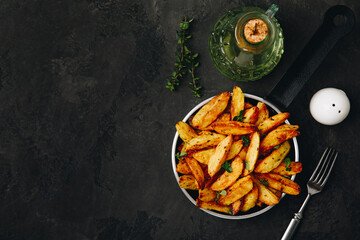 Roasted potatoes. Baked potato wedges in frying pan on dark stone background.