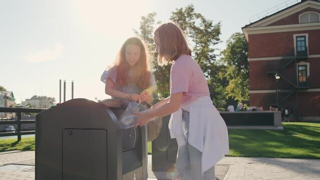 Teenage girls throw empty plastic bottles into recycling bin on school campus
