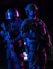 Fototapeta premium Modern warfare soldiers in dark with combat ammunition and weapons in the hands of equipped laser sights are in battle order. Mixed media. 