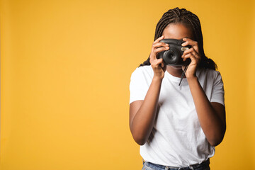 African-american woman taking photo of you. Female holding polaroid camera and pushing button standing isolated on yellow, making instant photo with retro camera