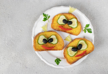 Frog-shaped croutons with cucumber, tomato and black olives on gray background - creative breakfast idea for kids