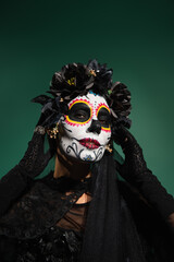 Woman with sugar scull halloween makeup touching face isolated on green.