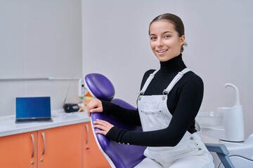 Fototapeta premium Portrait of young smiling teenage girl in dental chair looking at camera