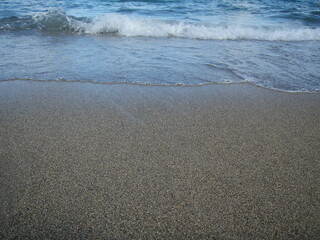 arena de playa recién mojada por el mar en retirada y olas con espuma llegando de nuevo a la orilla - obrazy, fototapety, plakaty