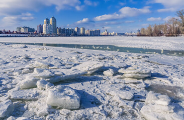 The Dnieper River is covered by ice and snow. The city district of Obolon appears in the background