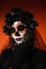 Portrait of woman in halloween costume and sugar skull makeup posing on red background.