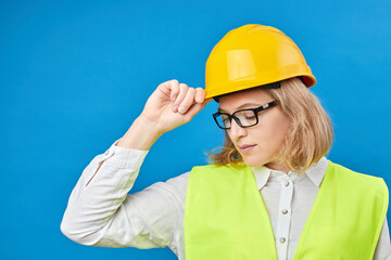 Young woman engineer wearing a yellow helmet, standing in studio on blue background. The concept of construction, repair, decoration. Studio shooting