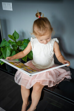 Happy cute little girl looking at photos in album. Happy smiling daughter browsing through printed family album, looking at pictures.