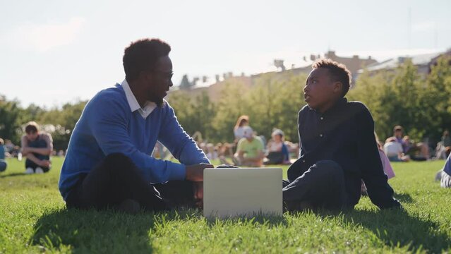 African-American male professor discussing exam results with student sitting on lawn near school