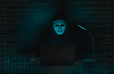 A hacker in black uses a laptop on a desk to hack a system with binary code.Cyber attack, system breaking and malware concept.