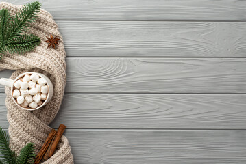 Fototapeta na wymiar Winter mood concept. Top view photo of mug of hot chocolate with marshmallow knitted scarf spruce branches anise and cinnamon sticks on grey wooden table background with empty space