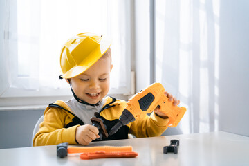 Fototapeta na wymiar Child play with work tools at home, dreams to be an engineer. Little boy builder. Education, and imagination, purposefulness concept. Kid and drill