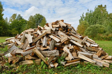 A large pile of firewood on the meadow. Trees has been cut and split into firewood to be used as fuel for heating in fireplaces and furnaces. Firewood pile. Shallow depth of field