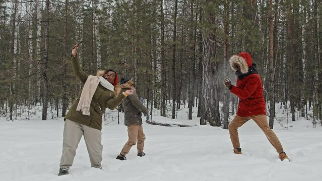Slow motion long shot of cheerful Black woman taking photos of her family playing snowballs on snowy winter day
