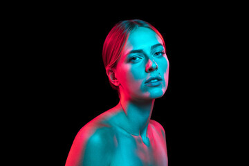 Closeup portrait of young pretty woman with naked shoulders in red neon light on dark background....