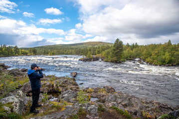 Hiker  in forest near river and looking trough binoculars