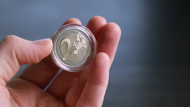 A woman hand holds and shows 2 euro coin in plastic case. Numismatist collecting a bi-metal coins. Rare collection copy. European money. Dark background.