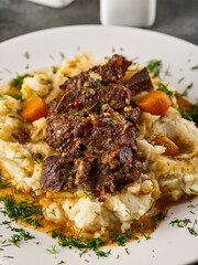 Beef cheeks with mashed potatoes on white plate.