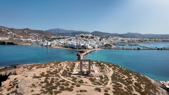 Aerial view of the famous Portara marble gate with the white houses of the city of Naxos island, Cyclades, Greece, during a sunny summer day