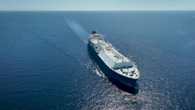 Aerial view of a large LNG or liquid gas tanker vessel traveling with high speed over blue ocean