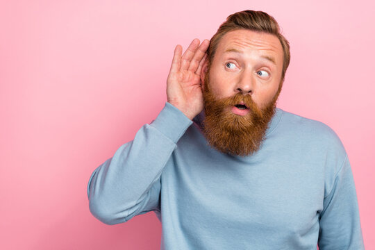 Photo of impressed astonished guy with ginger beard dressed blue sweatshirt arm ear look empty space isolated on pink color background