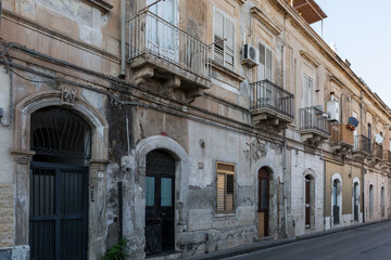 Shabby facade of an old Italian house with beautiful balconies and shuttered windows. Side view.