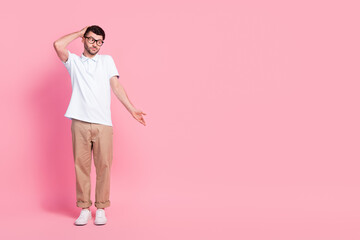 Full length photo of clueless attractive man stylish outfit look down arm direct empty space dont know isolated on pink color background