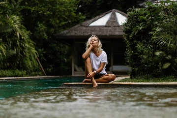 Swimming pool in a tropical villa. A young woman is sitting by the pool, enjoying the tranquility.