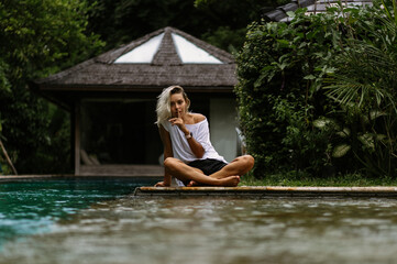 Swimming pool in a tropical villa. A young woman is sitting by the pool, enjoying the tranquility.