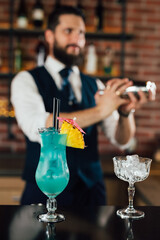 blue lagoon cocktail on bar counter, barman shaking cocktail in blurred background