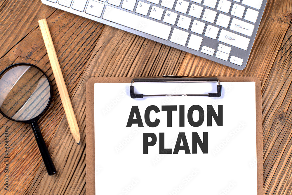 Poster action plan text on paper clipboard with magnifier and keyboard on wooden background