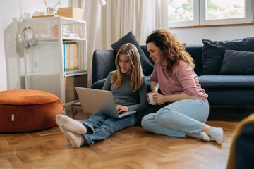 mother and teenage daughter using laptop in living room