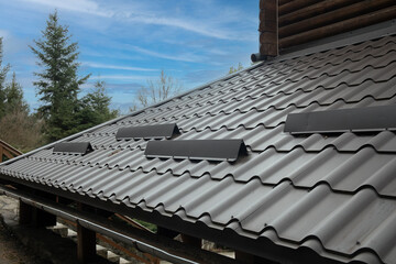 Closeup roof with metal grey shingle tiling surface with rain gutter pipe and snow guards protective fence.