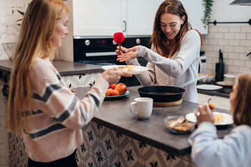 Young woman fries pancakes and treats her guests.