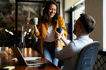 Colleagues laughing in office. Businesswoman and businessman drinking coffee.