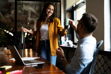 Colleagues laughing in office. Businesswoman and businessman drinking coffee.