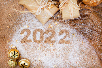 Fototapeta na wymiar Festive season 2022, snow with 2022 on rustic hessian surface with gifts and jingle bells