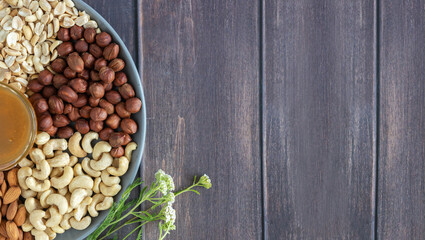 Flat plate with mixed nuts, honey, flowers. Top view background with healthy snack on a wooden dark table