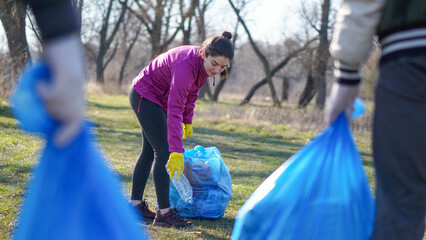 a young woman picks up a plastic bottle in the park. Ecology concept. © Marijana