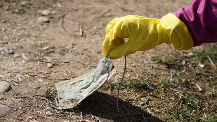 female hand with protective glove picking up an old protective mask from the ground. Pollution. Ecology concept.