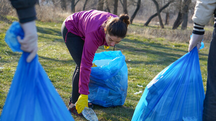 Young girl picking up plastic bottle with protective glove on Earth day at the park. Ecology...